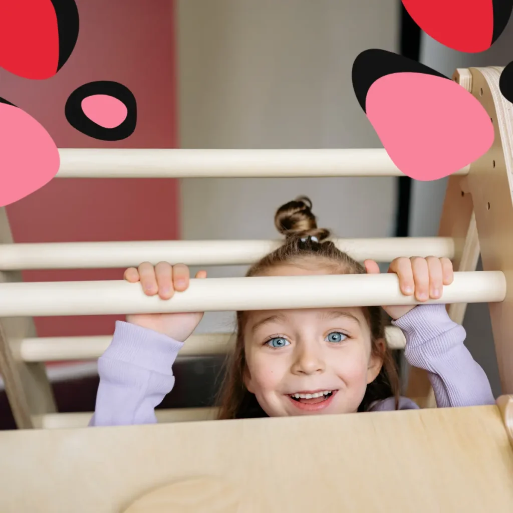 girl on montessori climbing toy peeking over the bars