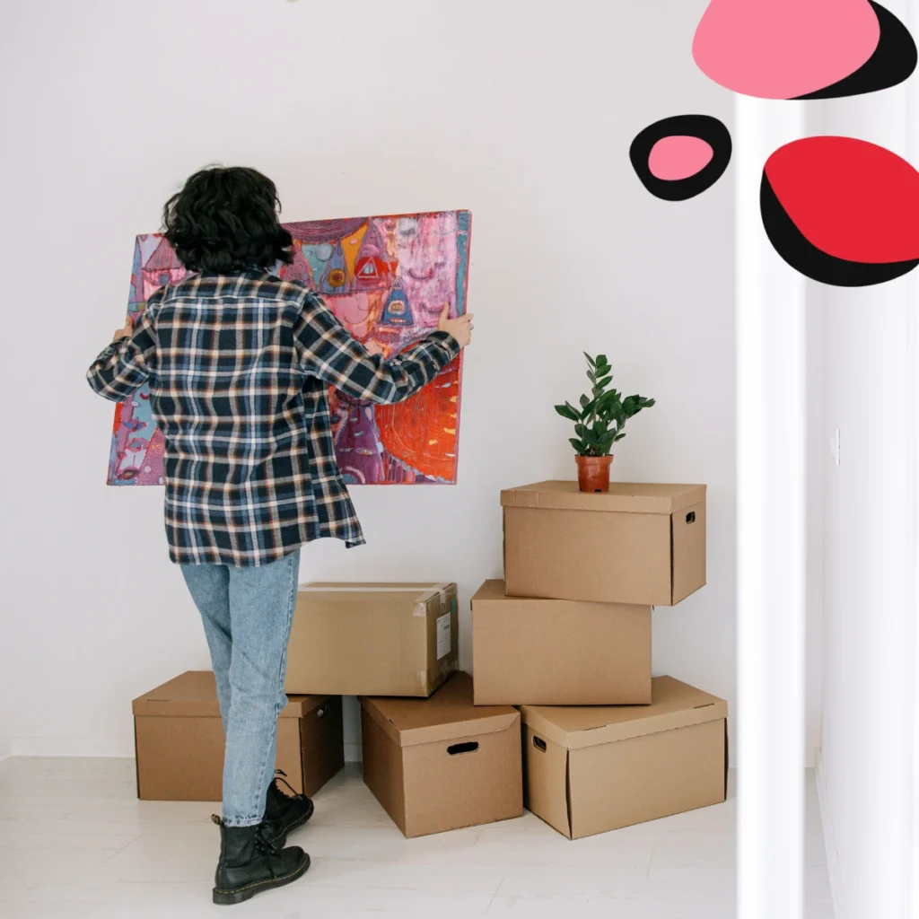 woman moving house with boxes and about to hang a colourful picture on the wall